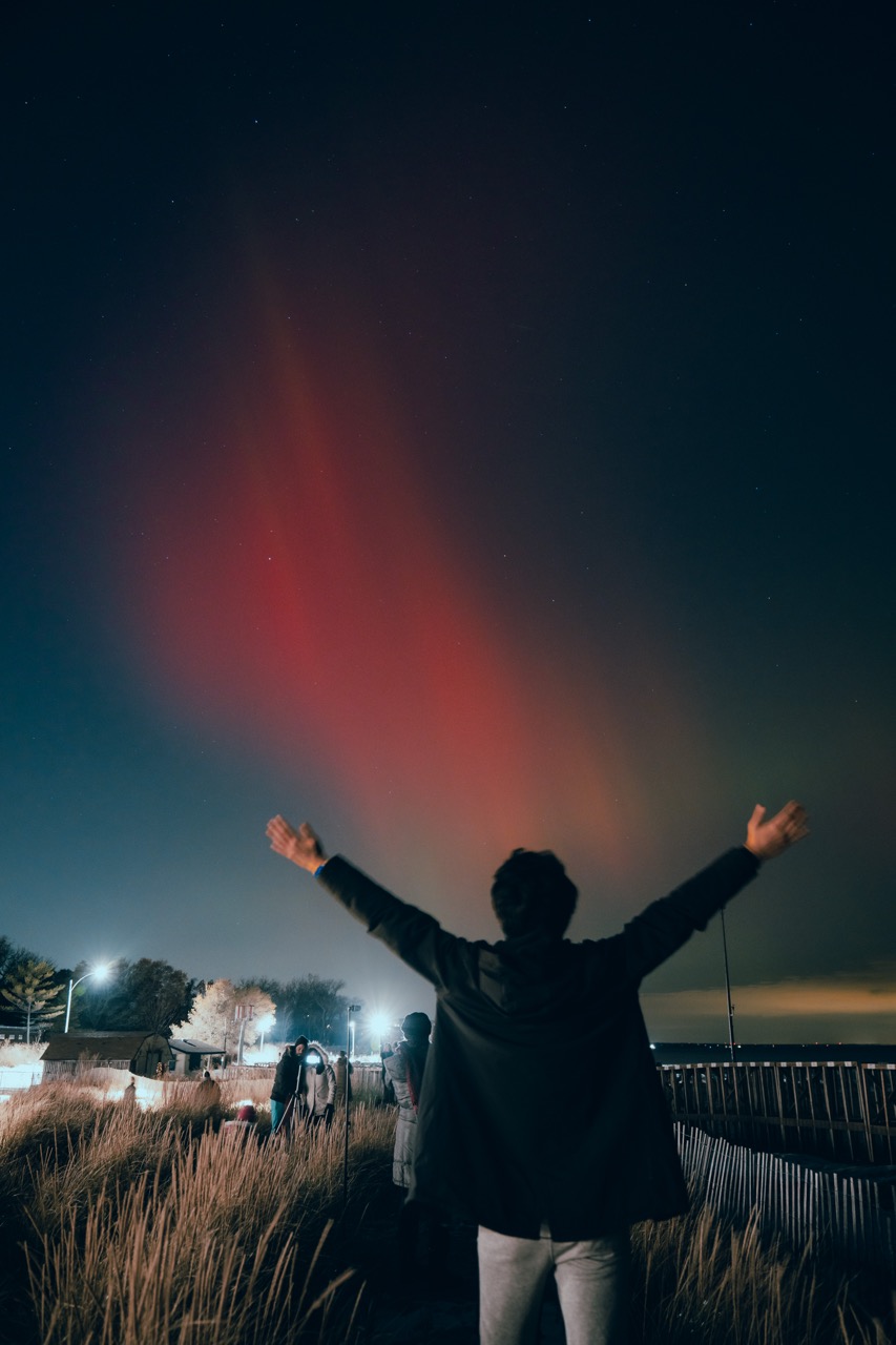 Person raising arms under a crimson aurora in Wilmette, Illinois.
